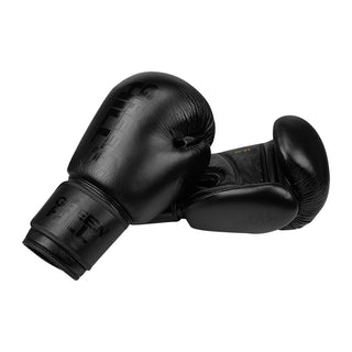 Ein Paar komplett mattschwarze Echtleder-Boxhandschuhe des Modells Tiger Black Edition von Green Hill vor weißem Hintergrund. Der linke Handschuh liegt im Vordergrund und zeigt den Handrücken sowie die Manschette mit einem dezenten, geprägten schwarzen Markenlogo. Der rechte Handschuh liegt leicht dahinter, sodass die Innenhand, der Daumenbereich und die goldene Unzen-Prägung '16 oz' sichtbar sind.