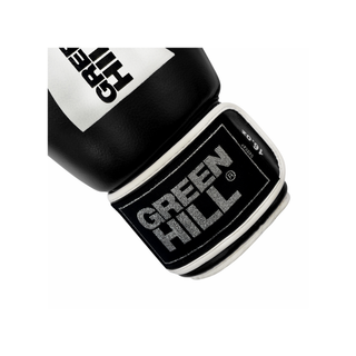 Nahaufnahme der Manschette eines schwarzen Green Hill Boxhandschuhs vor weißem Hintergrund. Im Fokus steht das rechteckige, schwarze Marken-Label auf dem Klettverschluss mit dem gestickten, silberfarbenen Green-Hill-Schriftzug. Am oberen Rand der Manschette ist die Unzen-Angabe '16 oz' zu sehen. Der Handschuh hat eine weiße Paspelierung (Randeinfassung).